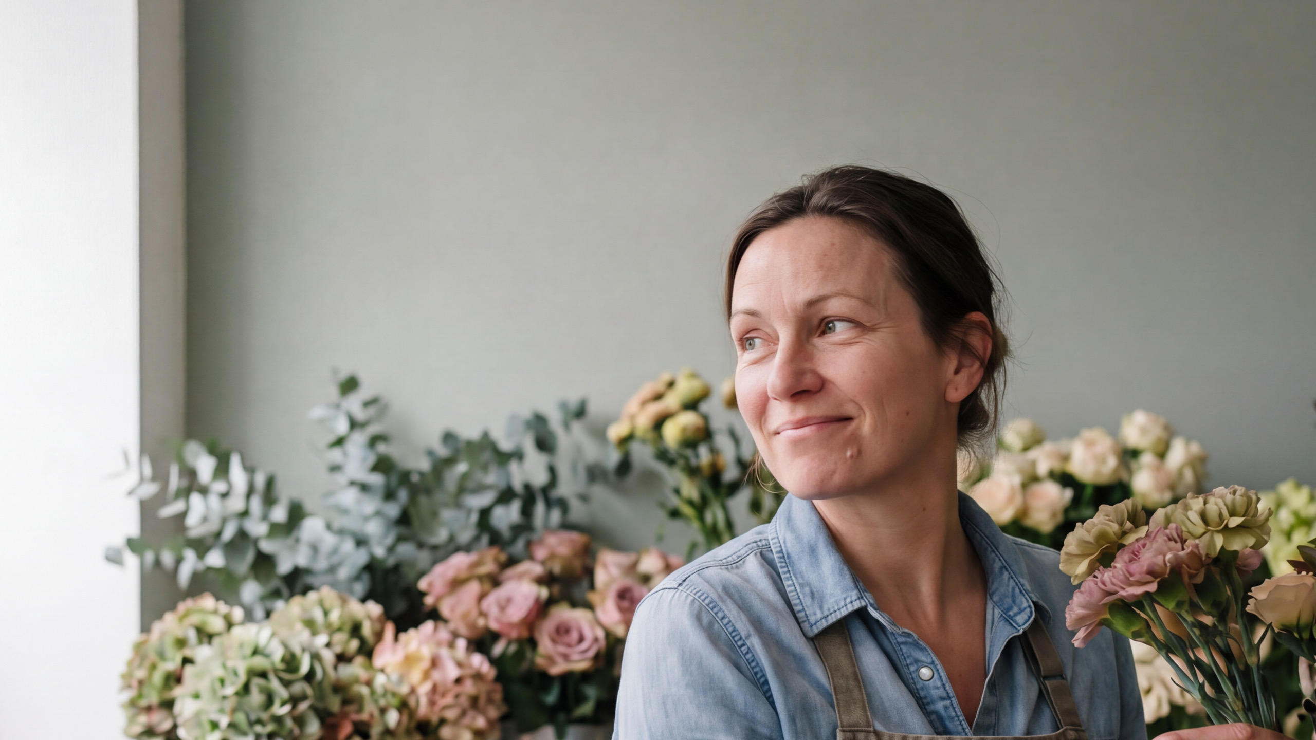 A florist smiling in her shop, surrounded by buckets of fresh flowers
