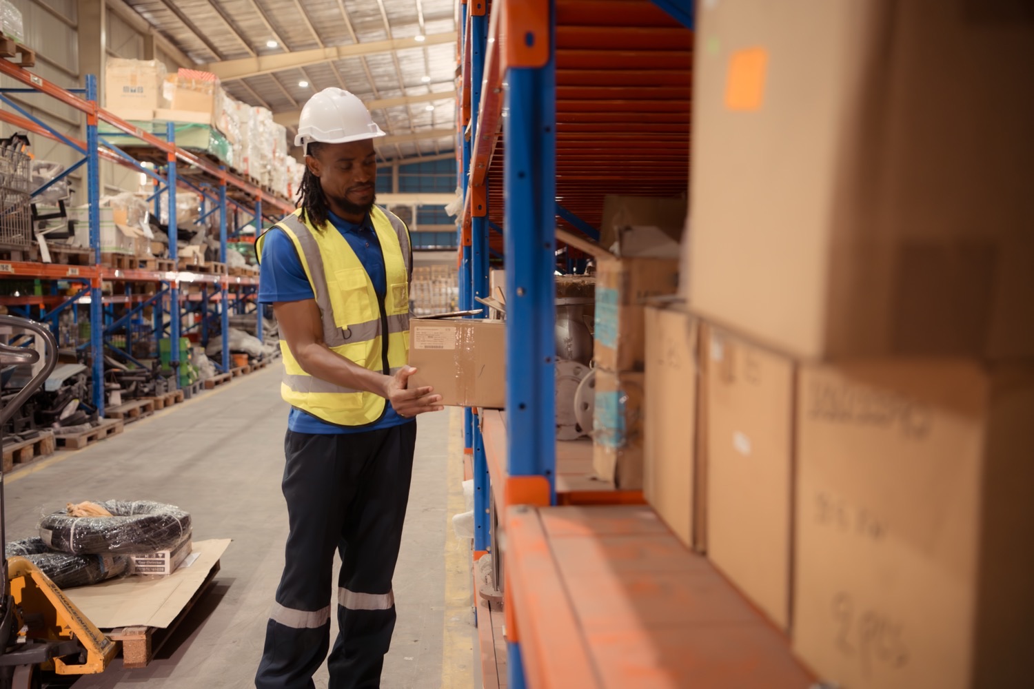 A warehouse worker in a hi-vis vest shelving a package in a small logistics operation